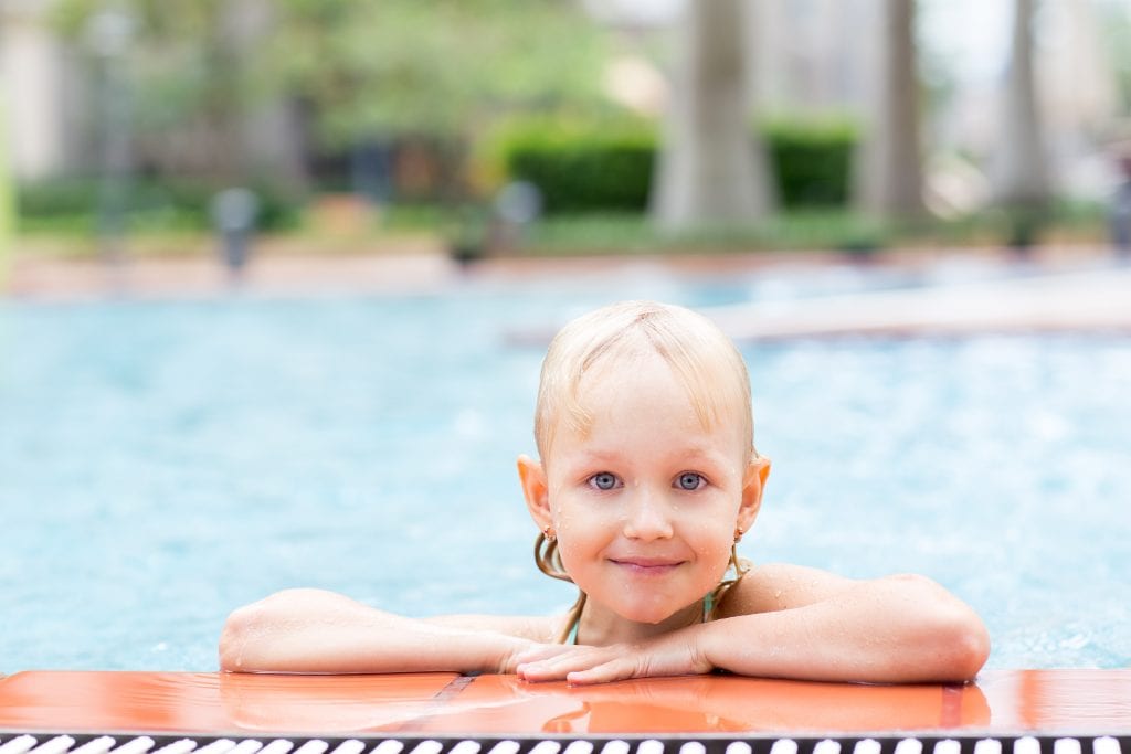 Portrait of happy little Caucasian girl resting in swimming pool, looking at camera and smiling during vacation. Summer, health and childhood concept